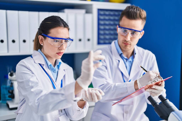 薬を持っている男性と女性の科学者は実験室で文書に書きます - 写真・画像
