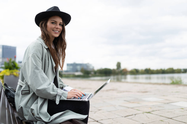 stylová mladá žena v klobouku pracuje na notebooku venku. - Fotografie, Obrázek