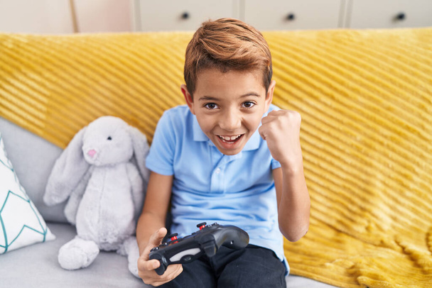 Αξιολάτρευτο ισπανόφωνο αγόρι που παίζει βιντεοπαιχνίδι καθισμένος στον καναπέ στο σπίτι - Φωτογραφία, εικόνα
