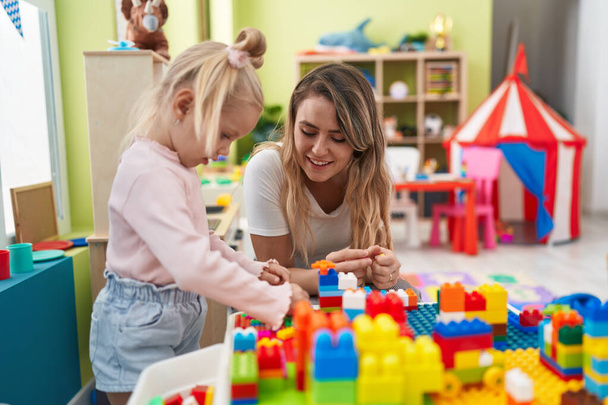 Учитель и ребенок играют со строительными блоками, сидя на столе в детском саду - Фото, изображение