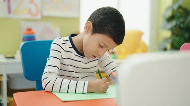 Uroczy Latynos chłopiec przedszkola student siedzi na stole rysunek na papierze w przedszkolu - Zdjęcie, obraz