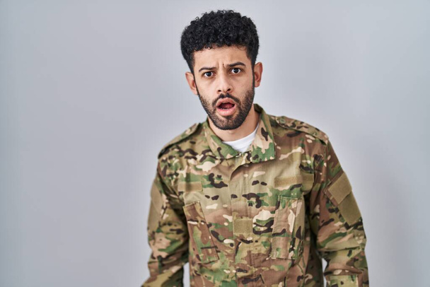 Arab man wearing camouflage army uniform in shock face, looking skeptical and sarcastic, surprised with open mouth  - Foto, imagen