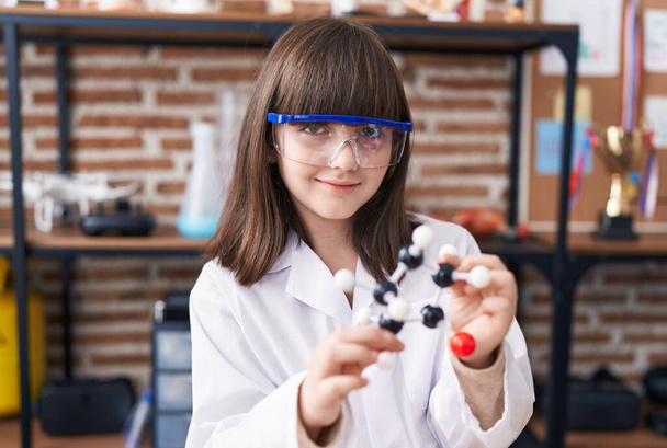 Adorable estudiante hispana sosteniendo moléculas en el aula de laboratorio - Foto, Imagen
