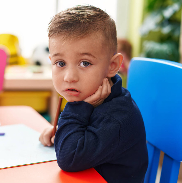 Adorable garçon hispanique élève préscolaire assis sur la table dessin sur papier à la maternelle - Photo, image