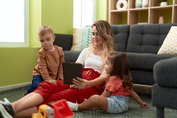 Kobieta z dziewczyną i chłopcem za pomocą touchpad siedzi na podłodze w domu - Zdjęcie, obraz