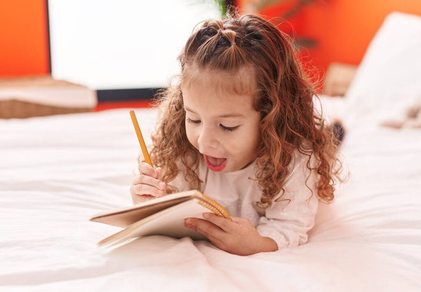 Adorabile bionda bambino scrivere su notebook sdraiato sul letto in camera da letto - Foto, immagini