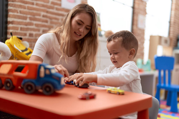 Teacher and toddler playing with cars toy sitting on table at kindergarten - Фото, изображение