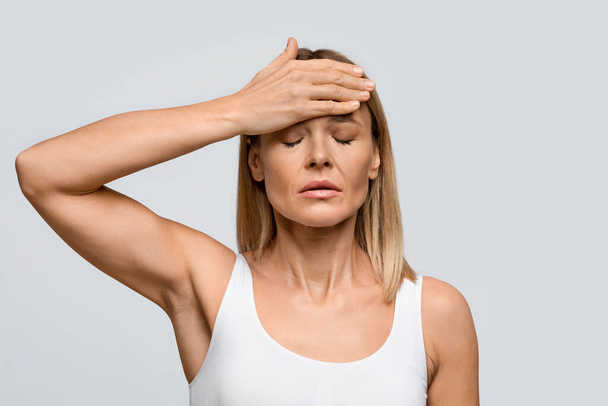 Unhappy sick middle aged blonde woman suffer from terrible strong head pain, touching her forehead with closed eyes, studio shot, lady have fever during cold, flu, coronavirus, influenza, copy space - Photo, Image