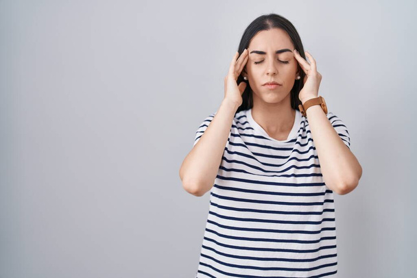 Genç esmer kadın çizgili tişört giyiyor, eli başının üstünde, stres yüzünden başı ağrıyor. migren ağrısı.  - Fotoğraf, Görsel