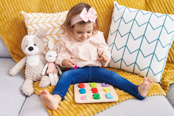 Очаровательный блондинка ребенок играет с математикой головоломка игра сидит на диване дома - Фото, изображение