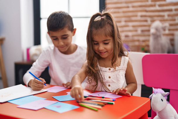 Estudiantes hermanos y hermanas sentados en mesa dibujando sobre papel en el jardín de infantes - Foto, Imagen