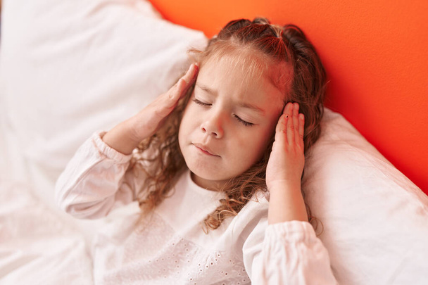 Liebenswertes blondes Kleinkind liegt auf Bett und leidet unter Kopfschmerzen im Schlafzimmer - Foto, Bild