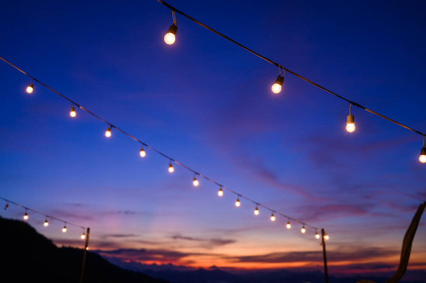 Festoon string lights decoration at the party event festival against sunset sky. light bulbs on string wire with copy space. Outdoor holiday background - Zdjęcie, obraz