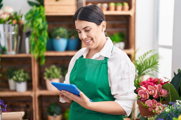 Young beautiful hispanic woman florist smiling confident using touchpad at flower shop - Fotoğraf, Görsel
