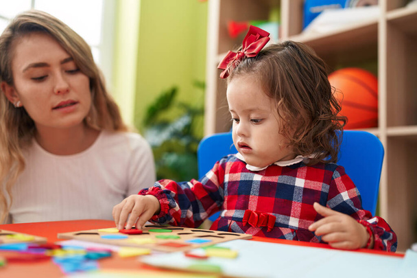 Вчитель і малюк грають з математикою головоломки, сидячи на столі в дитячому саду
 - Фото, зображення