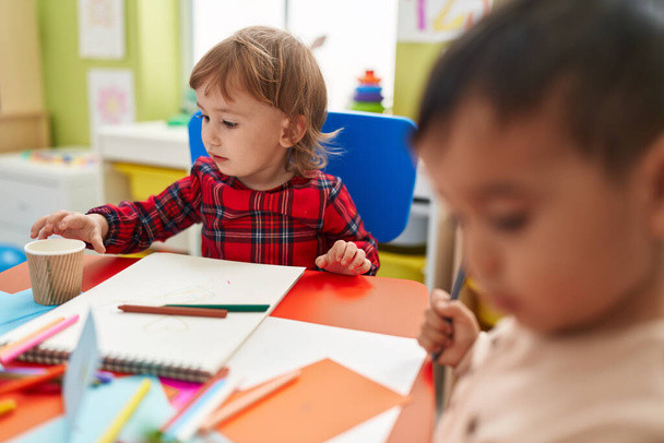 Двоє дітей дошкільного віку сидять на столі, малюючи на папері в дитячому садку
 - Фото, зображення