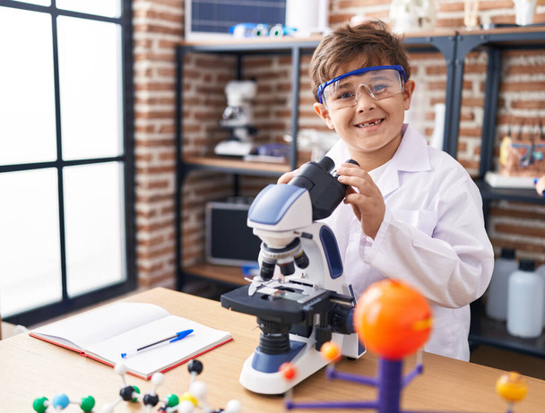 研究室の教室で顕微鏡を使って自信を持って微笑む愛らしいパニック少年 - 写真・画像
