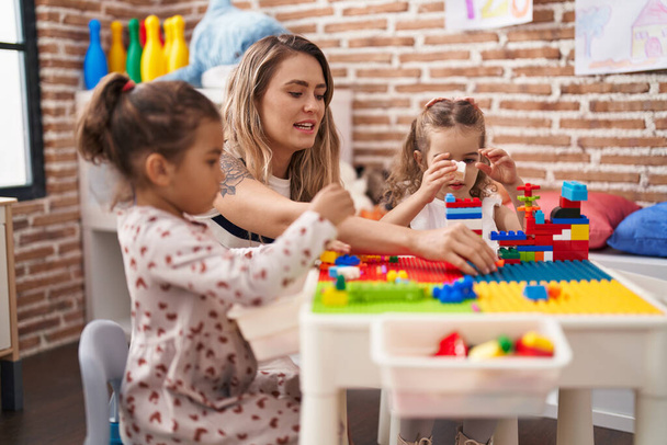 Учитель с девочками, играющими со строительными блоками, сидит на столе в детском саду - Фото, изображение