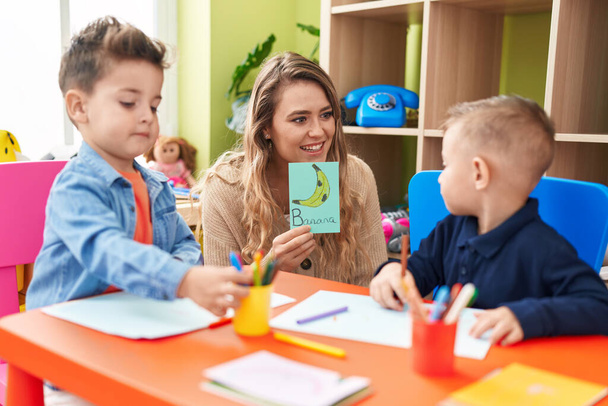 Учитель с мальчиками, сидящими на столе и занимающимися языками в детском саду - Фото, изображение