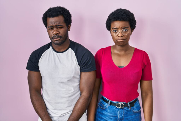 Genç Afro-Amerikan çifti pembe arka planda depresif ve endişeli, kızgın ve korkmuş bir şekilde duruyor. hüzünlü ifade.  - Fotoğraf, Görsel