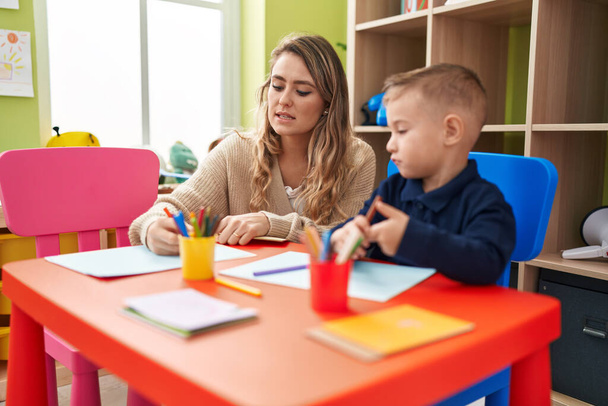 Teacher and toddler sitting on table drawing on paper at kindergarten - Fotó, kép