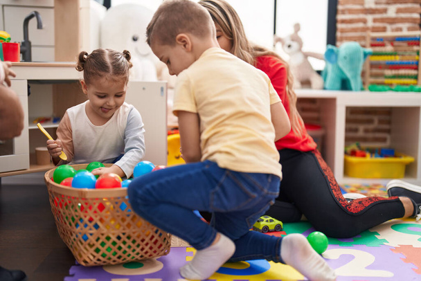 Lehrerin mit Jungen und Mädchen spielt im Kindergarten mit Bällen auf dem Boden - Foto, Bild