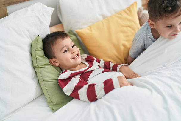 Δύο παιδιά χαμογελούν με αυτοπεποίθηση ξαπλωμένα στο κρεβάτι στην κρεβατοκάμαρα - Φωτογραφία, εικόνα