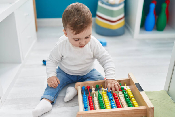 Schattige blanke baby spelen met abacus zitten op de vloer op de kleuterschool - Foto, afbeelding
