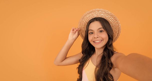 Yazın hasır şapkalı mutlu genç kız turuncu arka planda özçekim yapıyor, fotokopi çekiyor, selfie çekiyor.. - Fotoğraf, Görsel