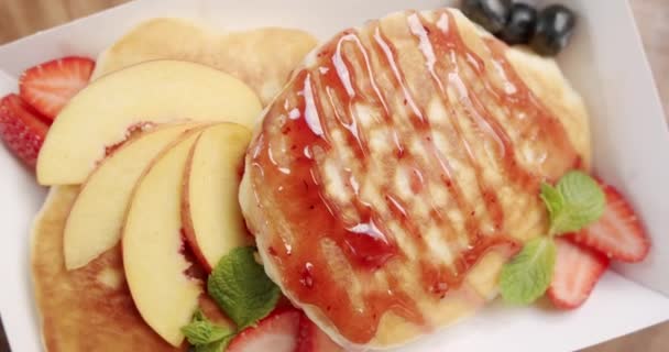 Amerikaanse karnemelkpannenkoeken met bosbessen, perzik, muntbladeren, aardbeien en ahornsiroop. Lekker zoet ontbijt. gezond eten ontbijt. versheid en gezondheidsvoeding. - Video