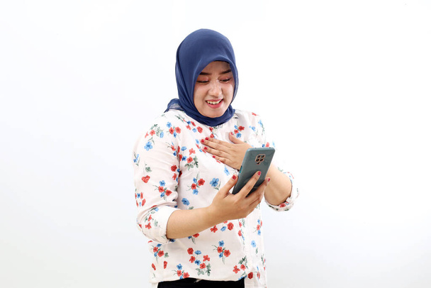 Happy asian muslim woman standing while holding a cell phone. Isolated on white background - Photo, image