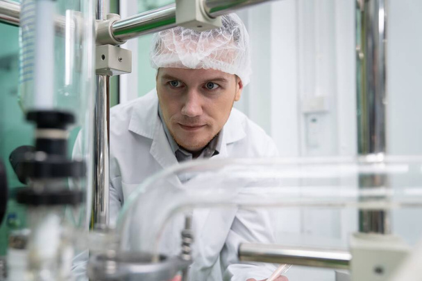 Porträt eines Wissenschaftlers, der in einem Labor mit einer Glasröhre Cannabisöl für den Flüssigkeitsfluss extrahiert. Cannabis-Extraktion für alternatives medizinisches Behandlungskonzept. - Foto, Bild