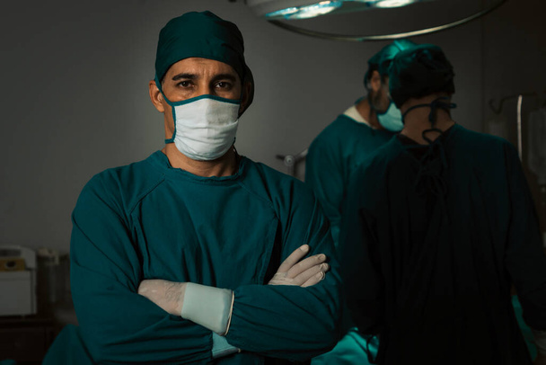 Porträt des chirurgischen Teamleiters im sterilen Operationssaal mit seinem Team und dem operierten Patienten. Selbstbewusster und professioneller Chirurg in voller Schutzkleidung versorgt seinen Patienten. - Foto, Bild