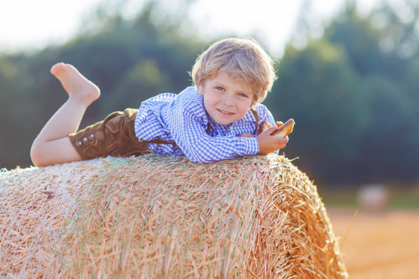 Funny little kid boy lying on hay stack  and smiling - Foto, afbeelding