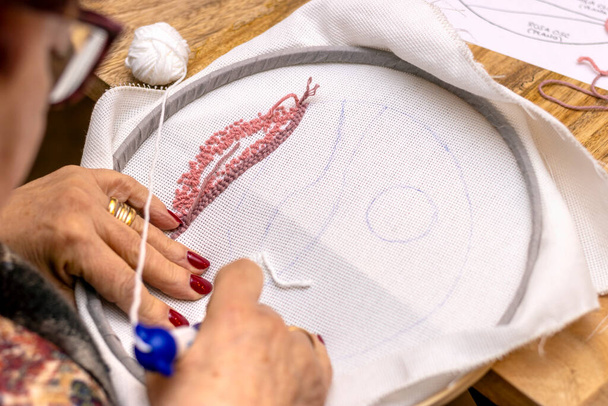 punch needle embroidery technique. Elderly woman embroidering with white wool. - 写真・画像