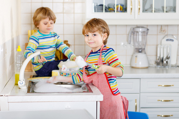 Due simpatici amichetti che lavano i piatti in cucina domestica
 - Foto, immagini