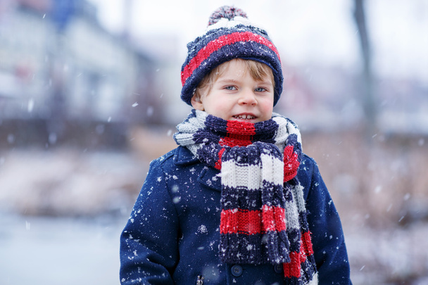 Χαριτωμένο μικρό αγόρι αστείο σε πολύχρωμα χειμερινά ρούχα διασκεδάζοντας με - Φωτογραφία, εικόνα