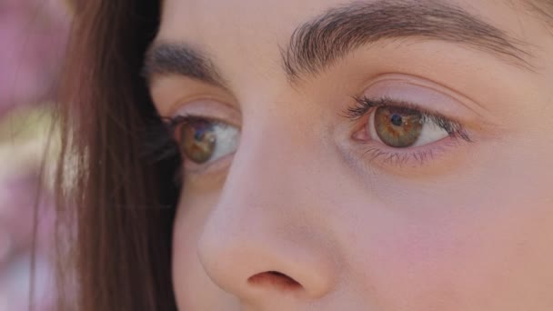 Young woman with dark eyes, lashes and eyebrows looking aside while standing on city street. Close up of female brunette girl with smooth healthy skin. - Video, Çekim
