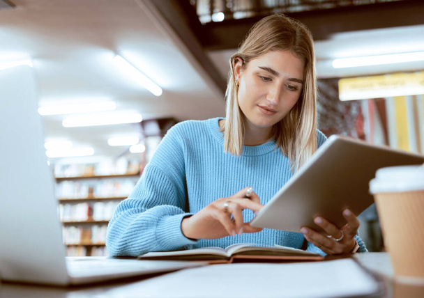 Education, university and woman in library with tablet, research and books for school project or exam. Laptop, notebook and internet, college student studying with technology and elearning on campus - Foto, Imagen
