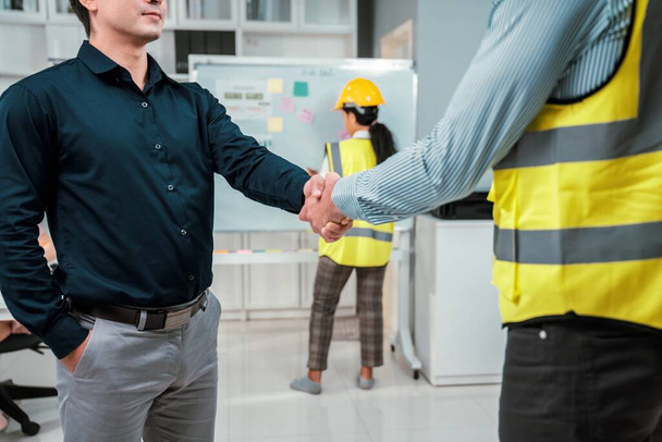 An engineer with a protective vest handshake with an investor in his office. Following a successful meeting, employee and employer form a partnership. - Fotografie, Obrázek