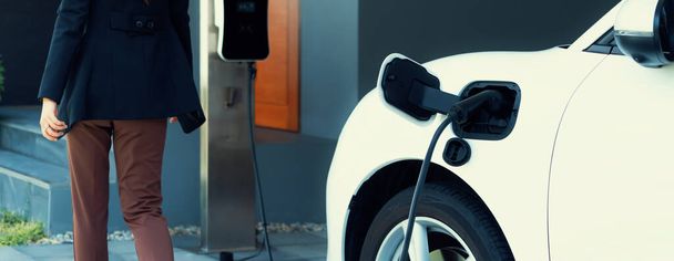 Progressive asian woman and electric car with home charging station. Concept of the use of electric vehicles in a progressive lifestyle contributes to a clean and healthy environment. - Foto, Imagen
