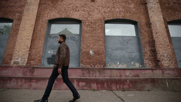 Udane szczęśliwy człowiek idzie na tle muru starej fabryki - Materiał filmowy, wideo