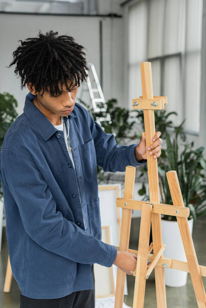 African american artist adjusting wooden easel in workshop  - Foto, imagen
