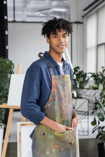 Kirli önlüklü genç Afrikalı Amerikalı sanatçı stüdyoda poz veriyor.  - Fotoğraf, Görsel