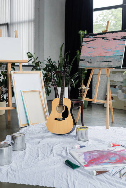 Acoustic guitar near paintings and paints in studio  - Foto, Imagen