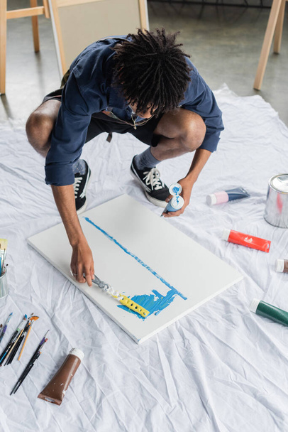Αφροαμερικανός καλλιτέχνης στην ποδιά ζωγραφική με σπάτουλα σε καμβά στο στούντιο  - Φωτογραφία, εικόνα