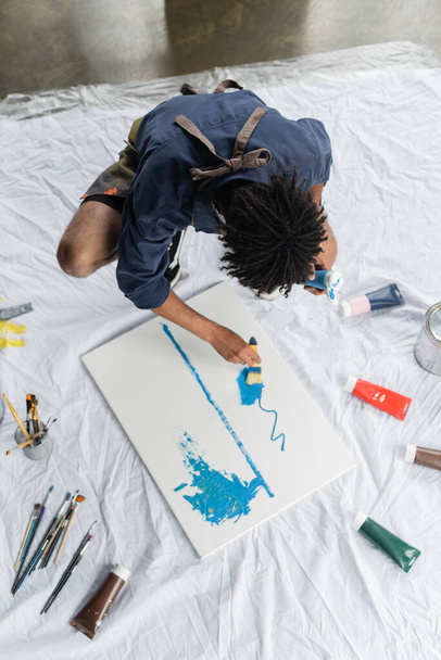 Overhead view of african american artist painting on canvas on floor in studio  - Фото, изображение