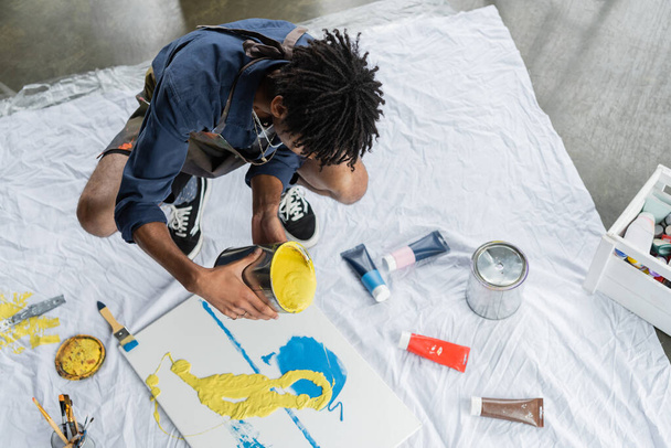 Overhead view of african american artist pouring paint on canvas in studio  - Fotó, kép