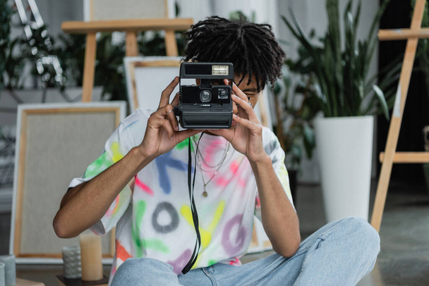 Artista afroamericano tomando fotos en cámara vintage en estudio  - Foto, Imagen