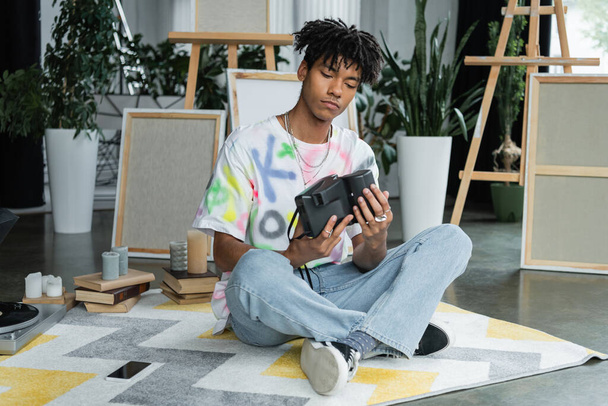 Artiste afro-américain tenant une caméra vintage près du smartphone et des livres en atelier  - Photo, image